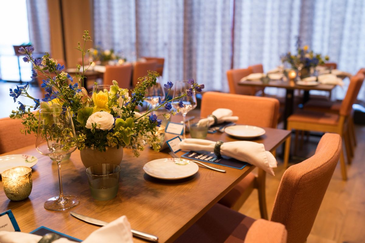 Elegant restaurant dining room with orange upholstered chairs around wooden tables set with plates, napkins.