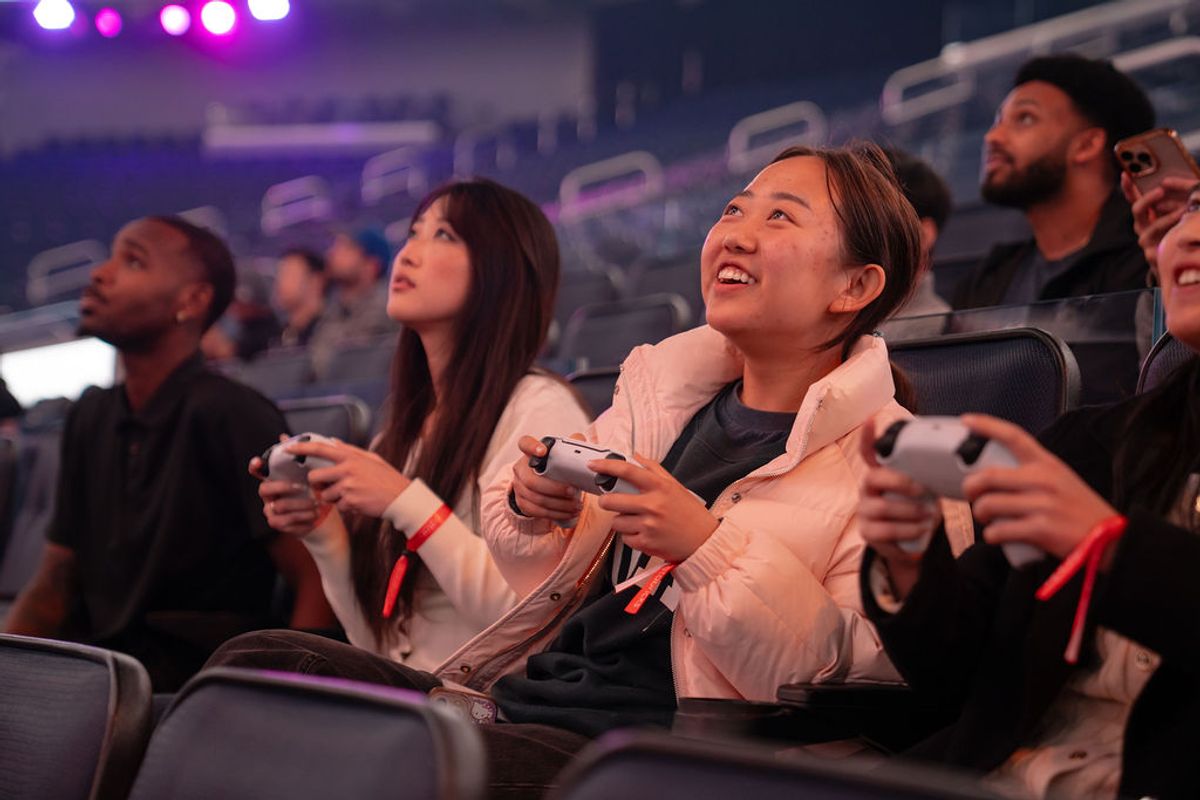 Attendees holding game controllers and smiling while looking up at screens during a gaming event