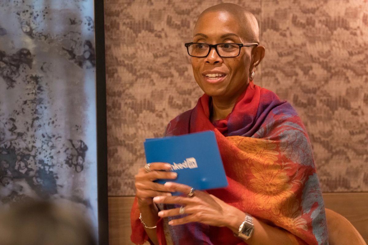 Panel speaker in colorful shawl holds blue book while seated at discussion event