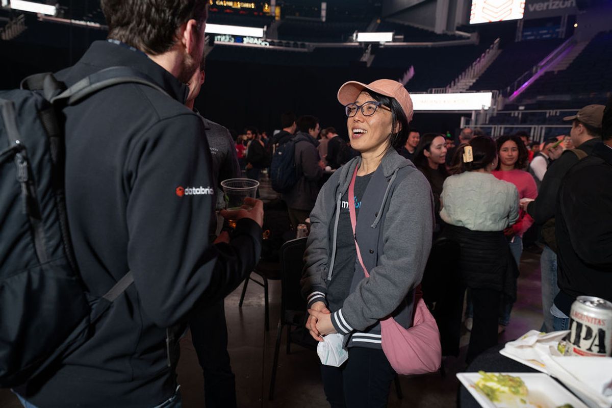 Two attendees networking at an indoor event, with one person wearing a pink cap and glasses talking to.