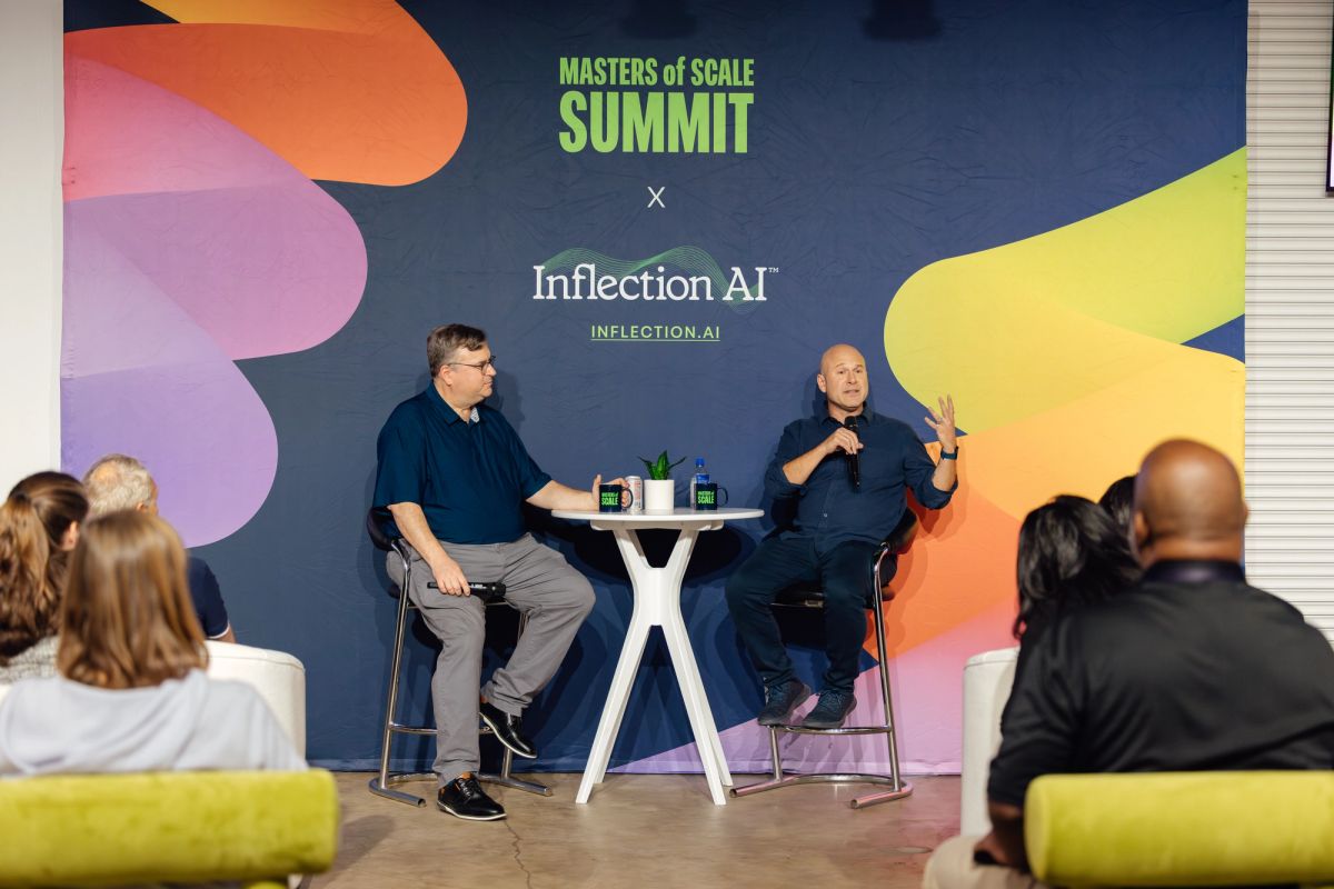 Two speakers on stage in chairs having a conversation at Masters of Scale Summit, with colorful backdrop and.