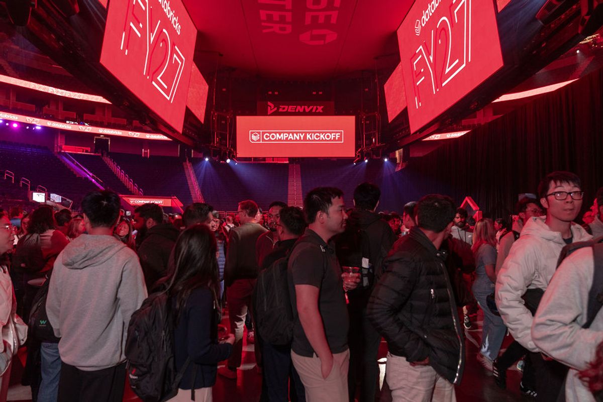 Attendees networking in red-lit arena with "COMPANY KICKOFF" displayed on overhead screen and hanging banners