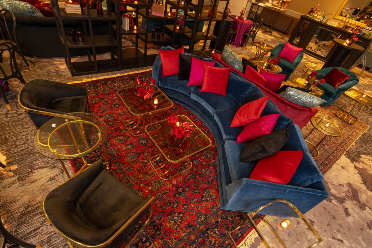 Curved blue sectional sofa with red and pink pillows around ornate red rug in upscale hotel lounge