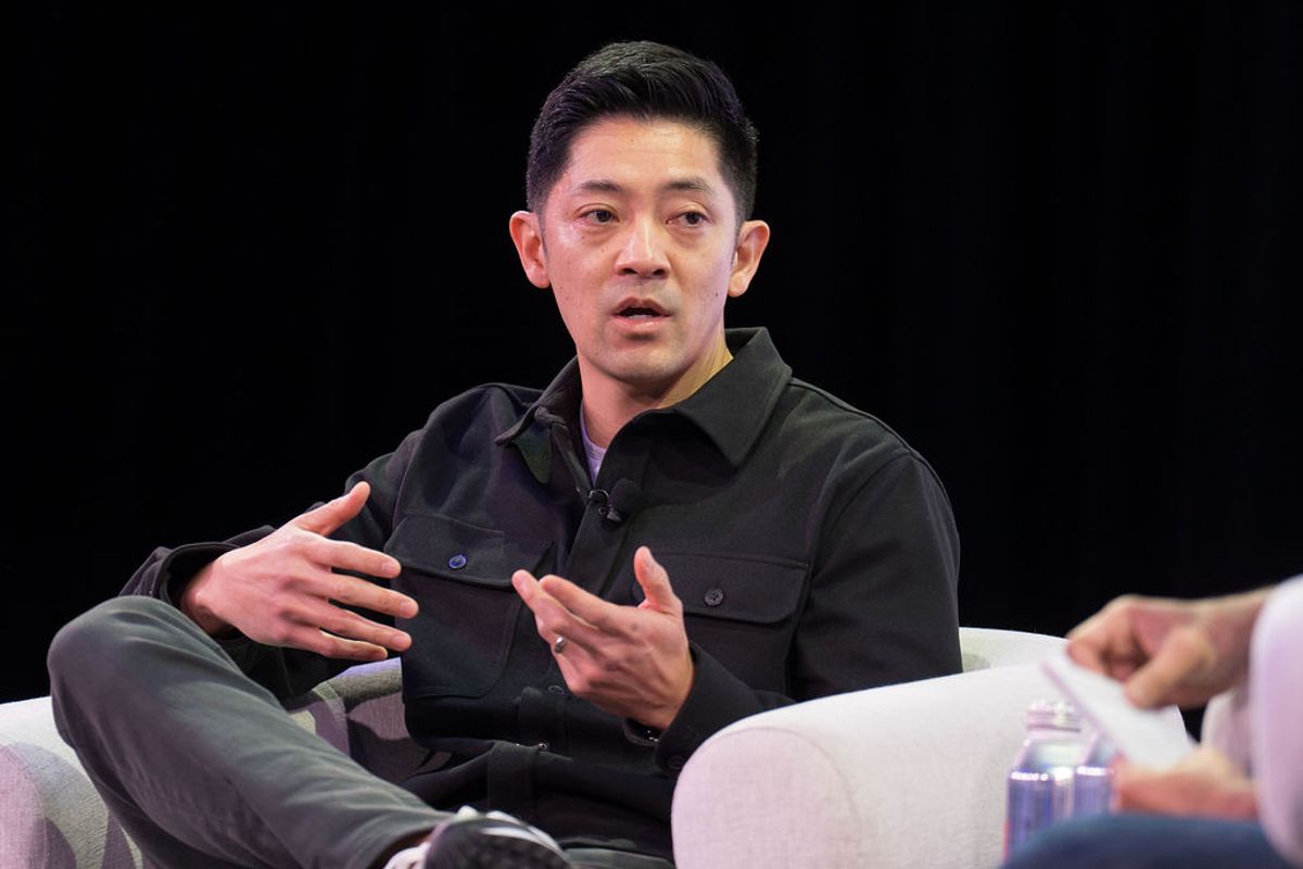 Speaker in dark shirt gesturing while seated during panel discussion at conference event