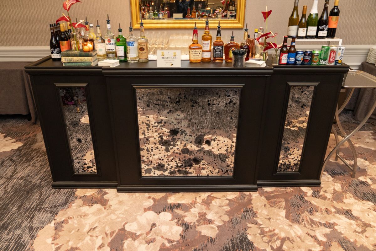 Bar setup with dark wood cabinet, mirrored panels, bottles of liquor and wine, with carpeted floor