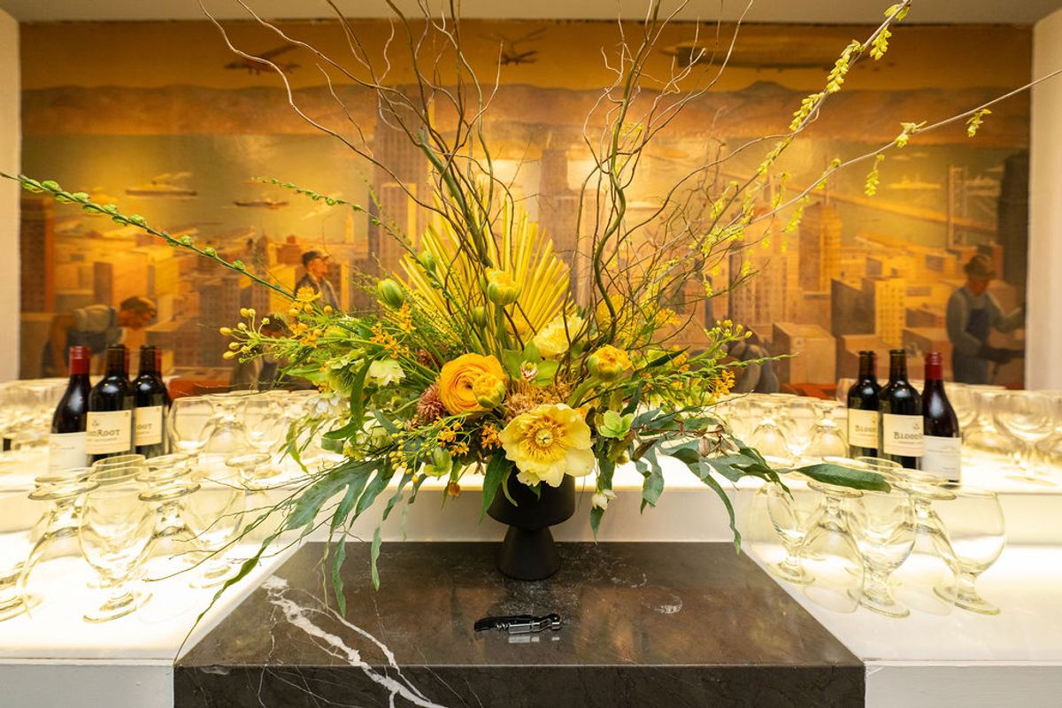 Large floral centerpiece with yellow flowers on table with wine bottles and glasses at networking event