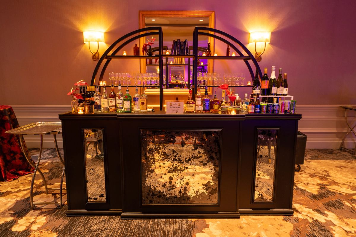 Elegant home bar setup with mirrored cabinet, liquor bottles, glassware, and warm ambient lighting