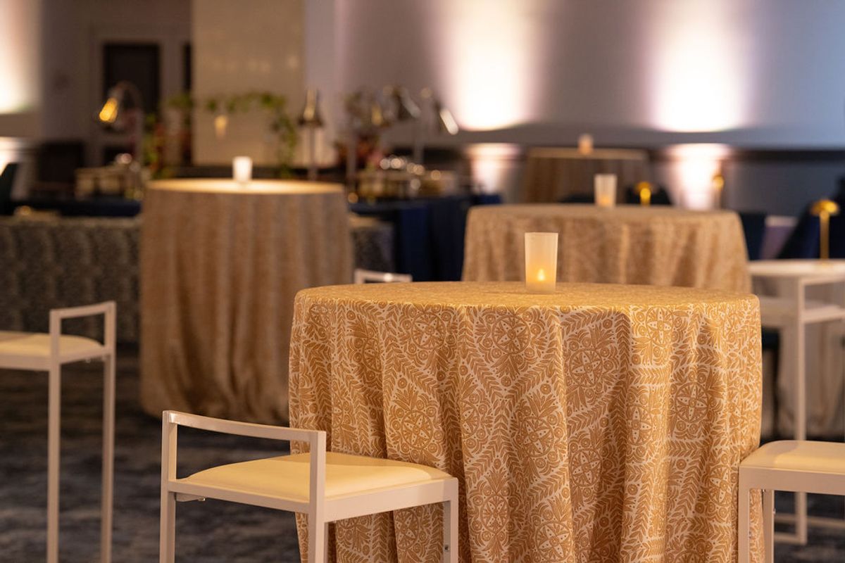 Cocktail tables with golden patterned tablecloths and modern chairs in an upscale event space with candles