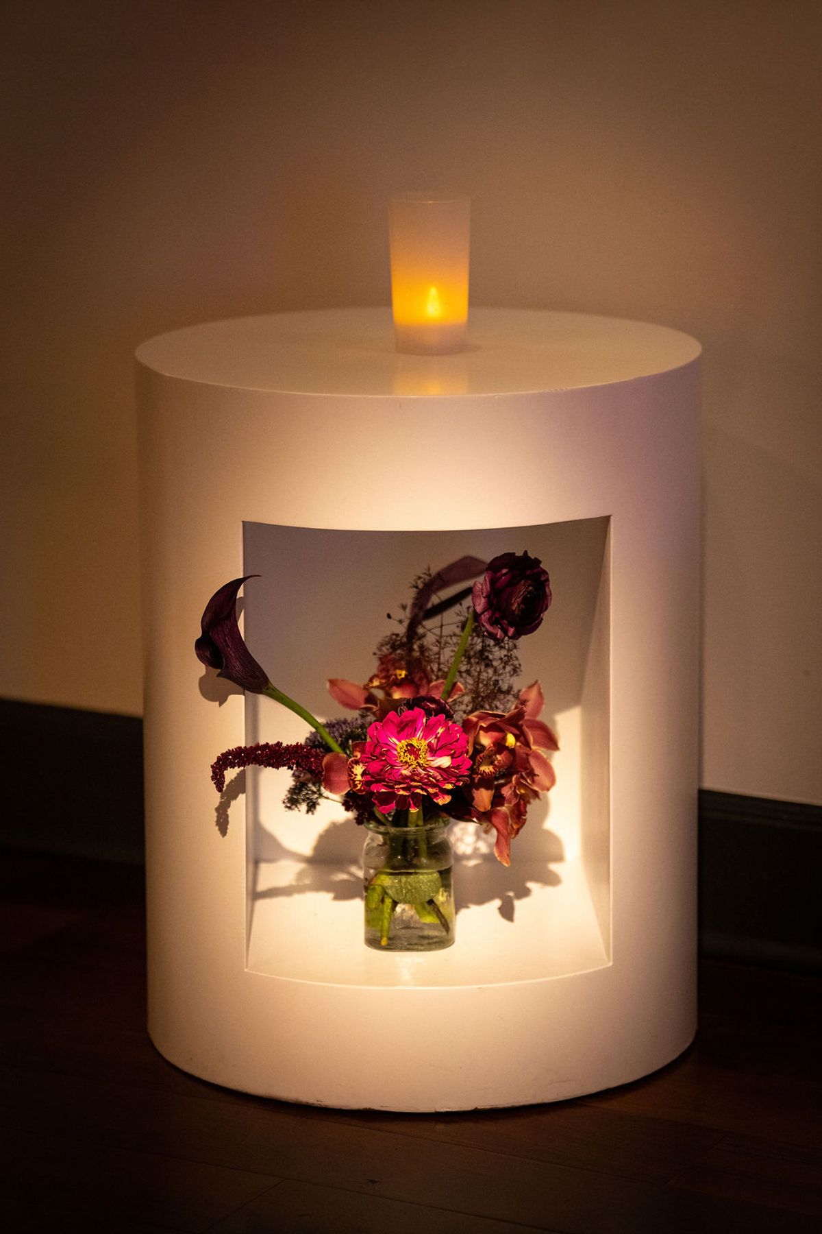 White cylindrical lamp with illuminated niche displaying colorful flower arrangement in small vase at.