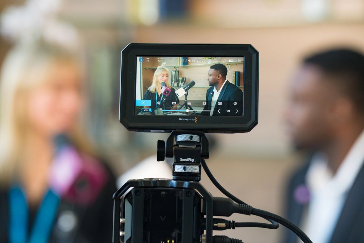 Camera monitor displays two people in conversation during a filming session with blurred subjects in.