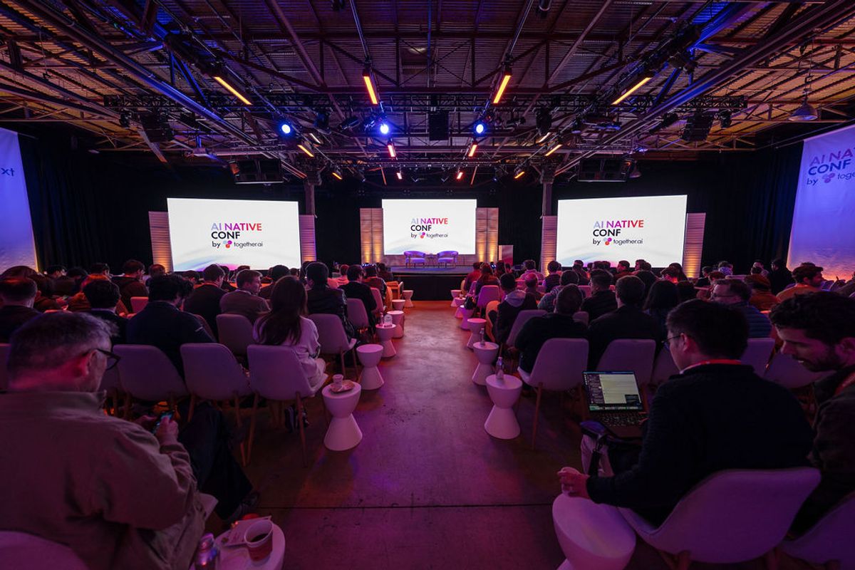 Attendees seated in auditorium facing stage with three screens displaying "CONATIVE CONF" branding under.