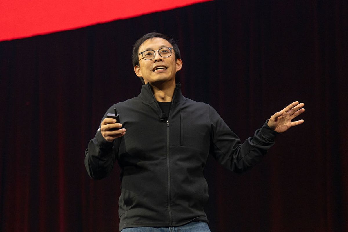 Speaker in glasses and dark jacket presenting on stage with hand gestures at conference event