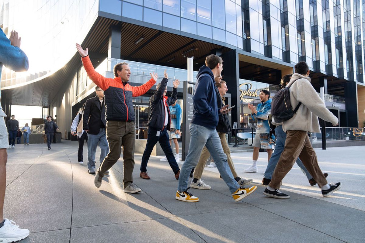 Group of conference attendees walking together outside modern glass building, one person celebrating with.