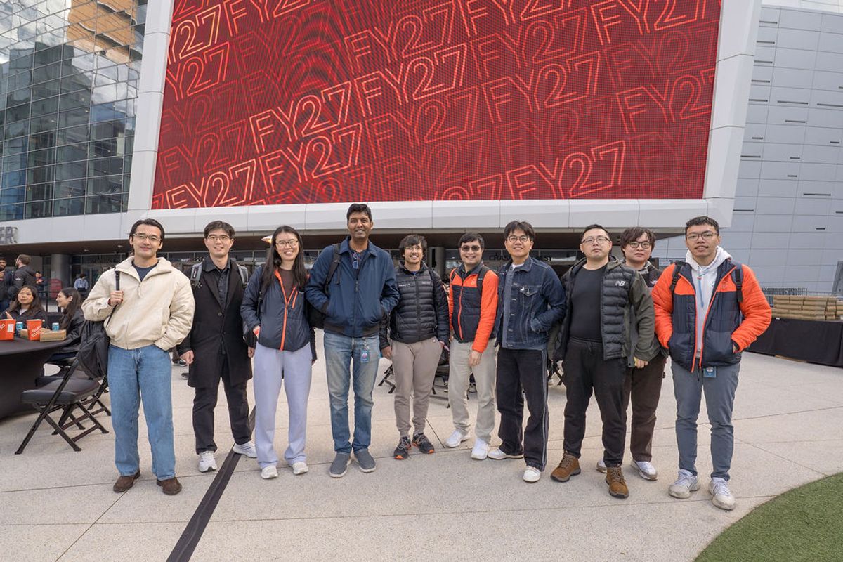 Ten people stand together for a group photo in front of a large red display showing "F27EV27F" text pattern.