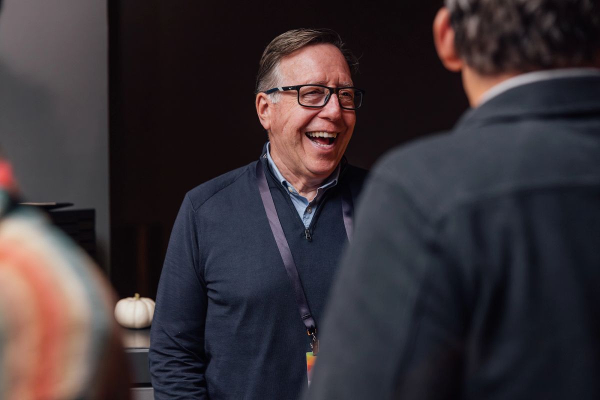 Man in glasses and navy sweater laughing while talking to another person at a conference event