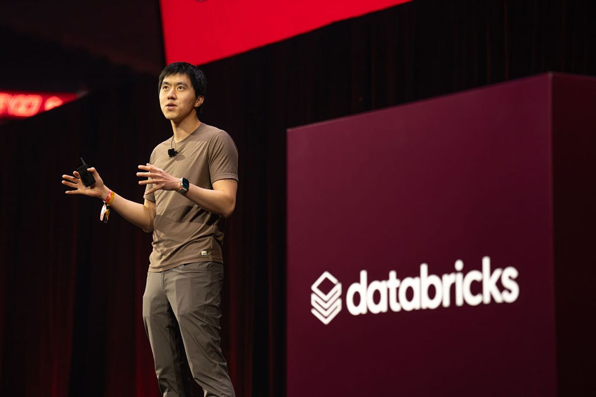 Speaker presenting on stage with Databricks logo backdrop at conference venue