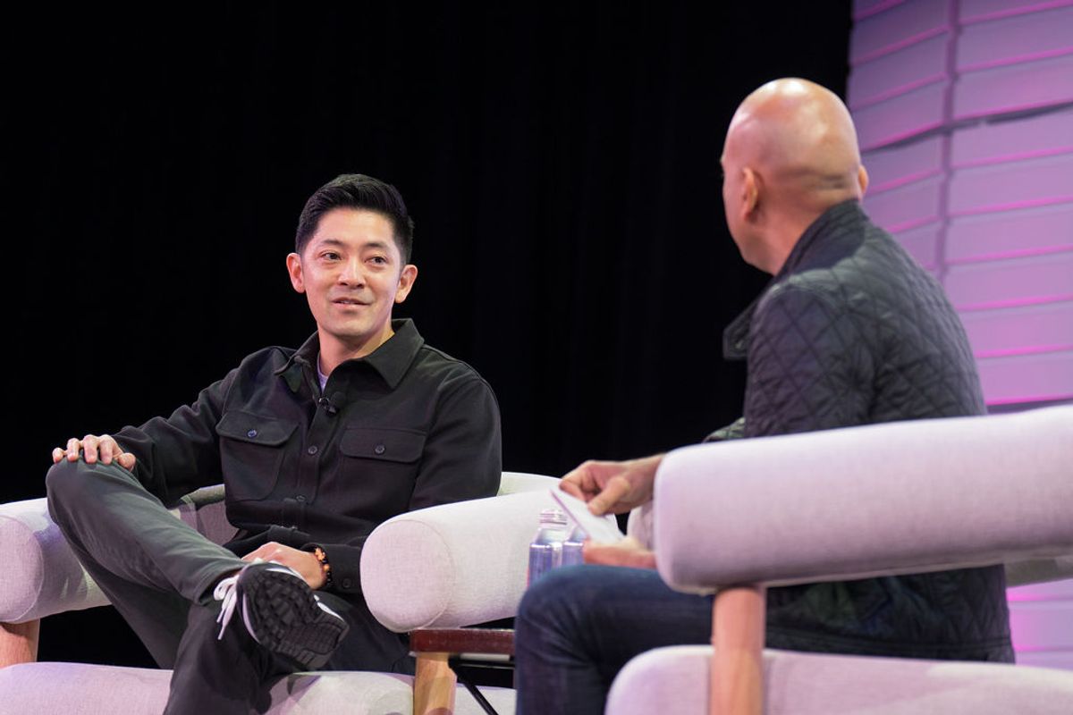 Two men in conversation on white curved chairs at a conference, one facing the camera in dark clothing