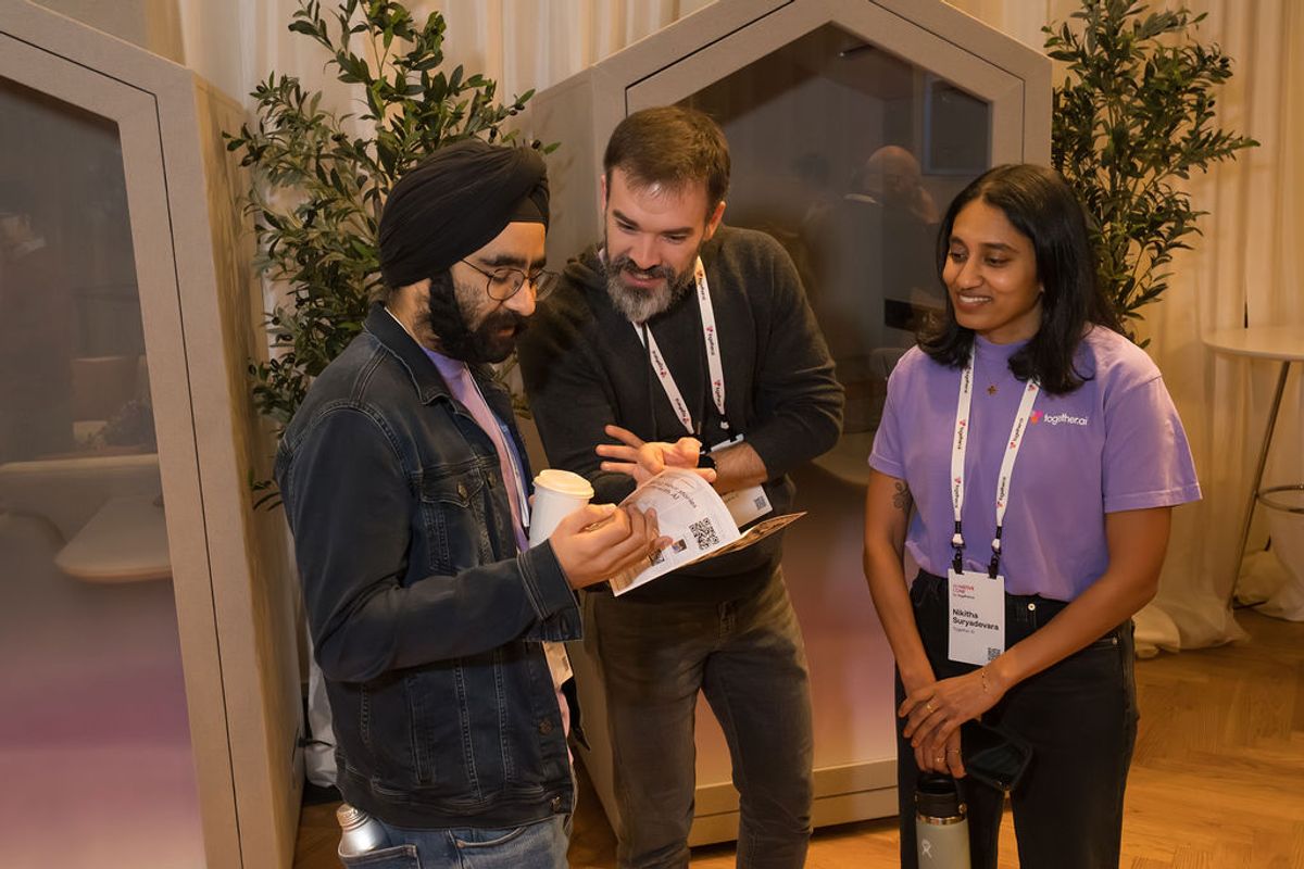 Three conference attendees with name badges examine a brochure together in a modern venue with plants and.