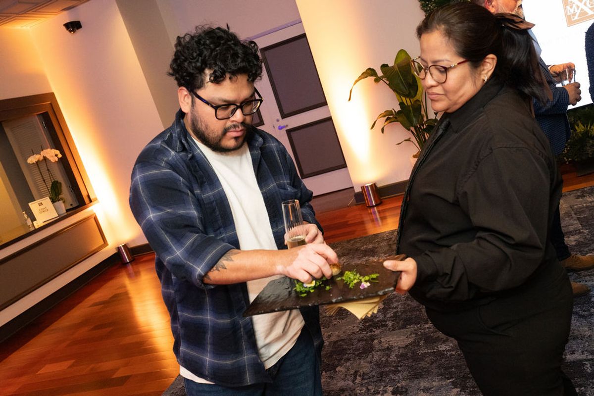 Two attendees networking and sharing food at an indoor reception event with modern decor and warm lighting.