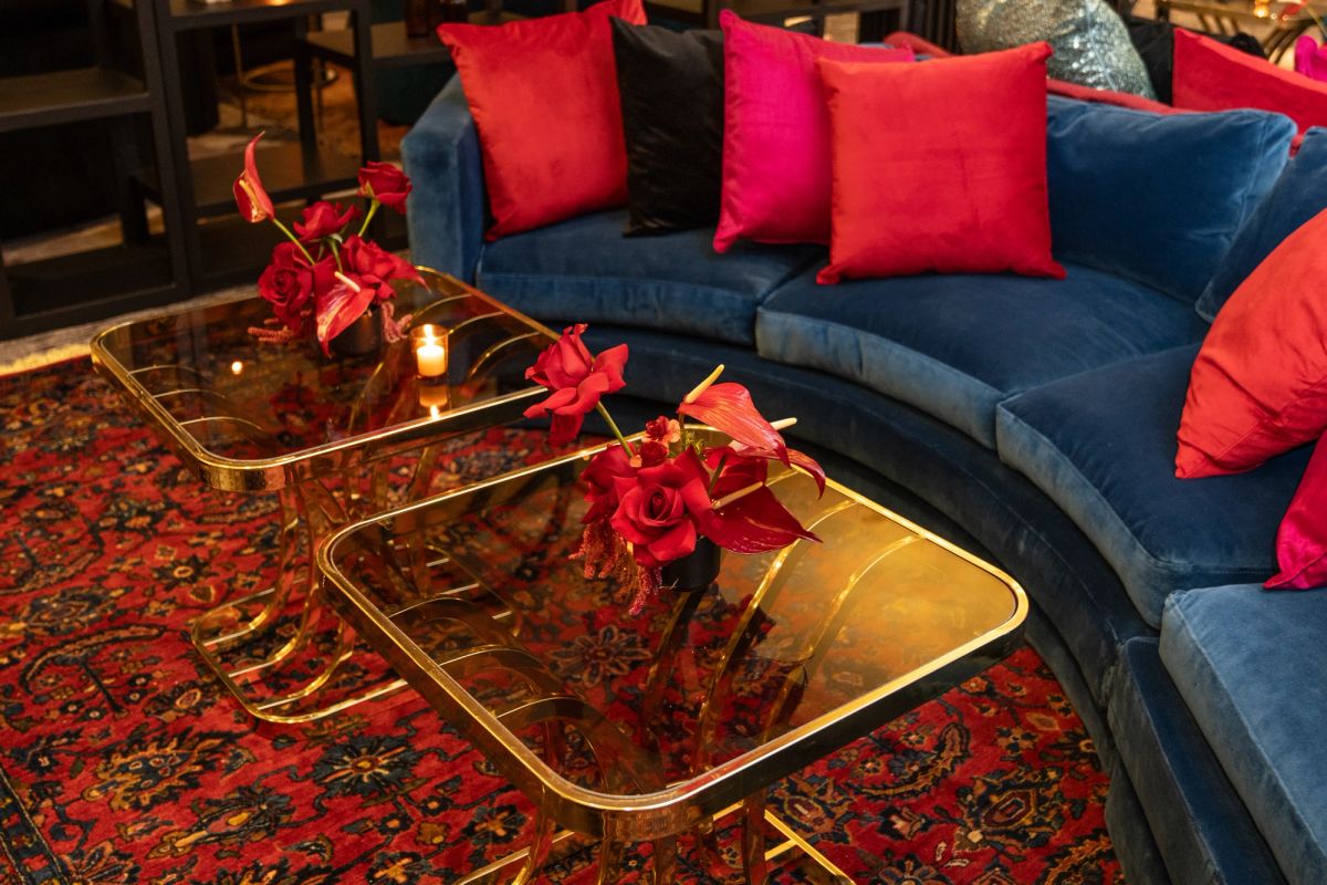 Blue velvet sofa with red pillows beside glass coffee table with red roses on patterned rug
