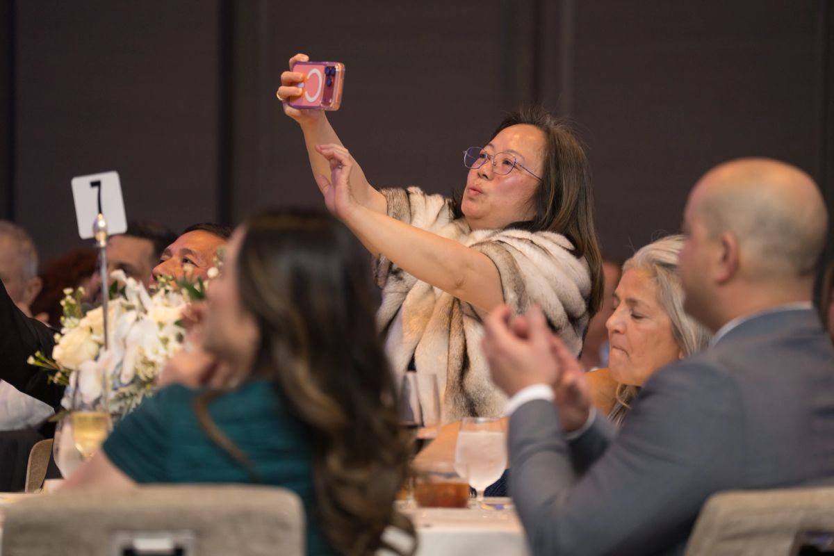 Woman taking selfie at formal dinner event while guests sit at decorated tables