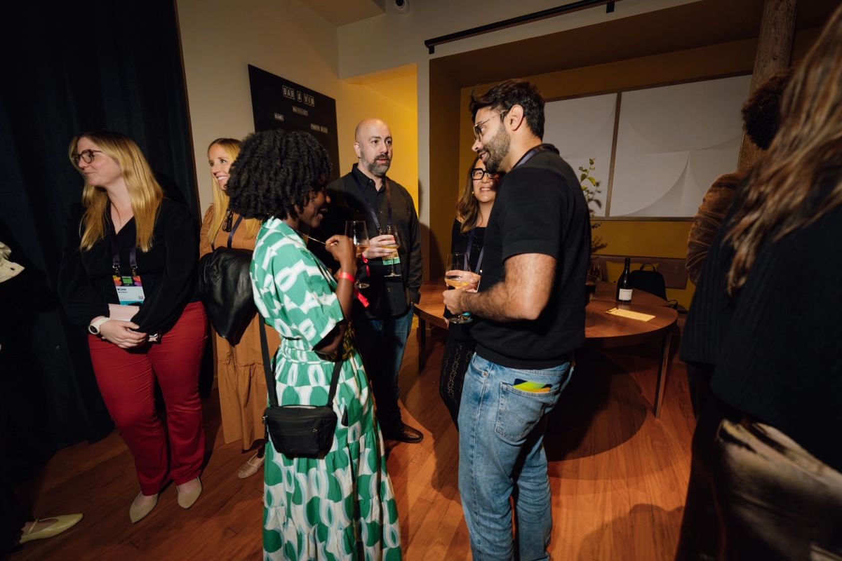 Attendees networking and conversing in a conference room with wooden floors and yellow accent wall