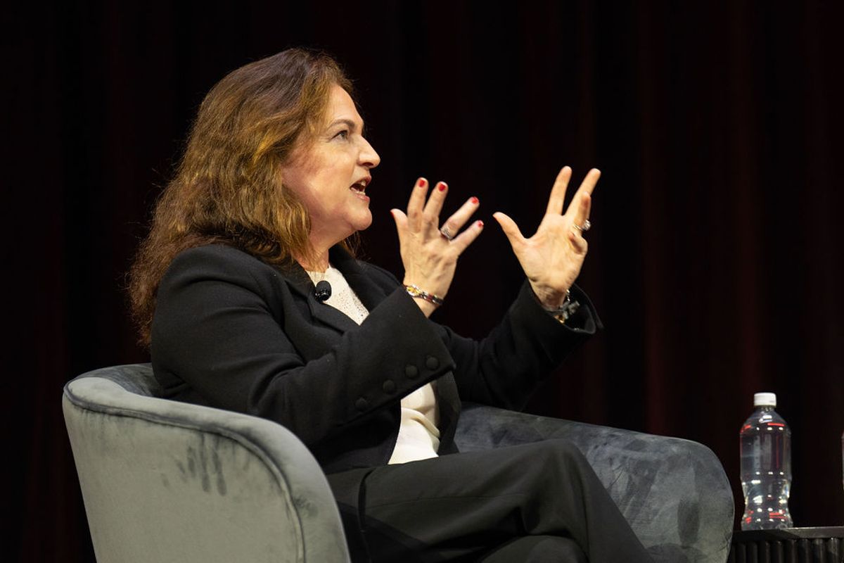 Two people in conversation on stage, one seated interviewer facing a casually dressed speaker in jeans and.