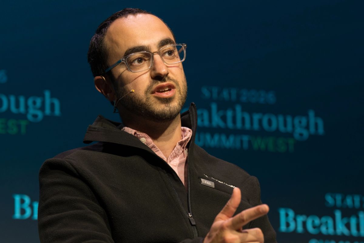 Speaker gesturing while presenting at conference with "Breakthrough" backdrop visible behind him