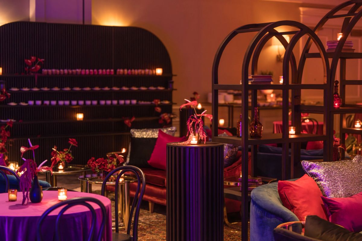 Dimly lit lounge with purple and orange ambient lighting, featuring modern furniture, small tables with.
