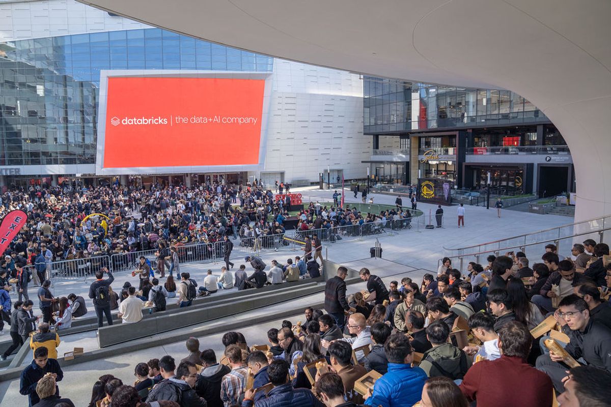Large crowd of attendees gathered in modern venue with Databricks signage displayed on screen above