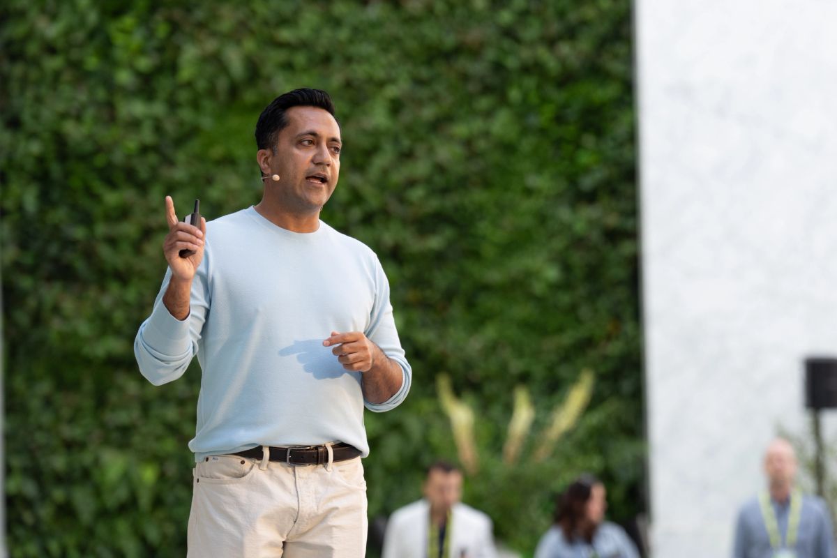 Speaker gestures while presenting outdoors before a lush green living wall backdrop.