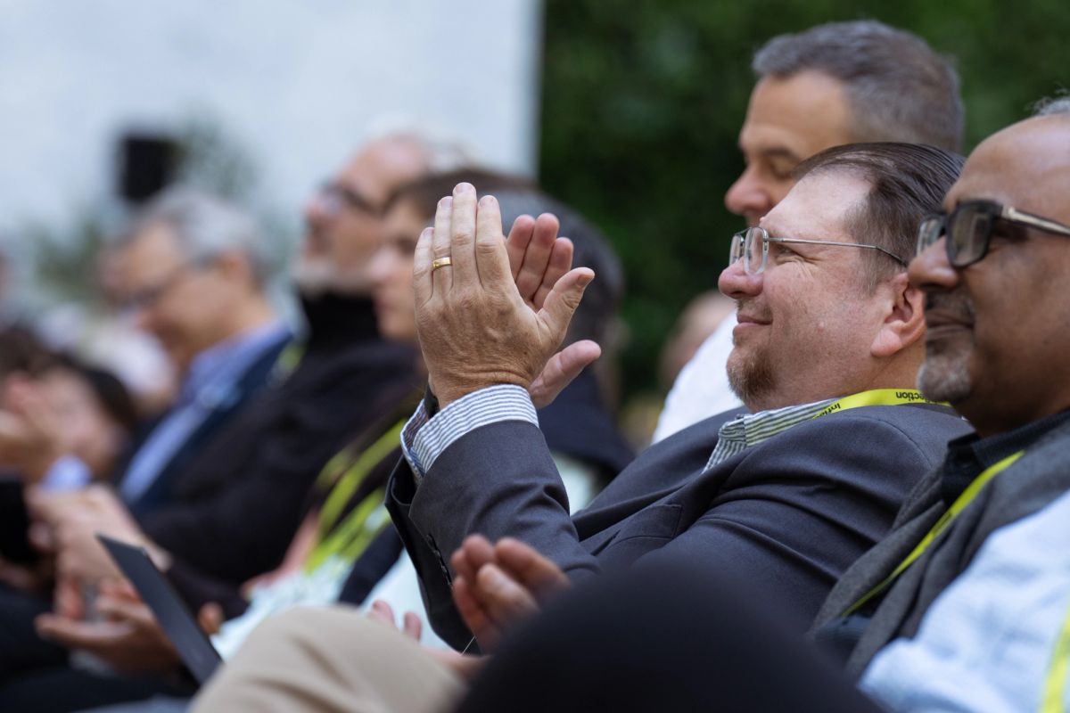 Attendees applauding at an outdoor conference, man in foreground clapping and smiling.