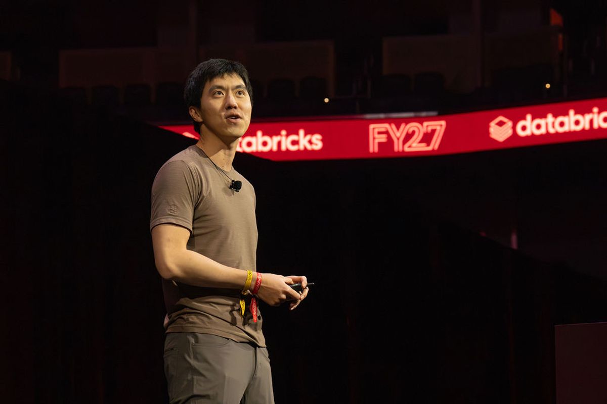 Speaker presenting on stage at Databricks conference with red illuminated signage in background