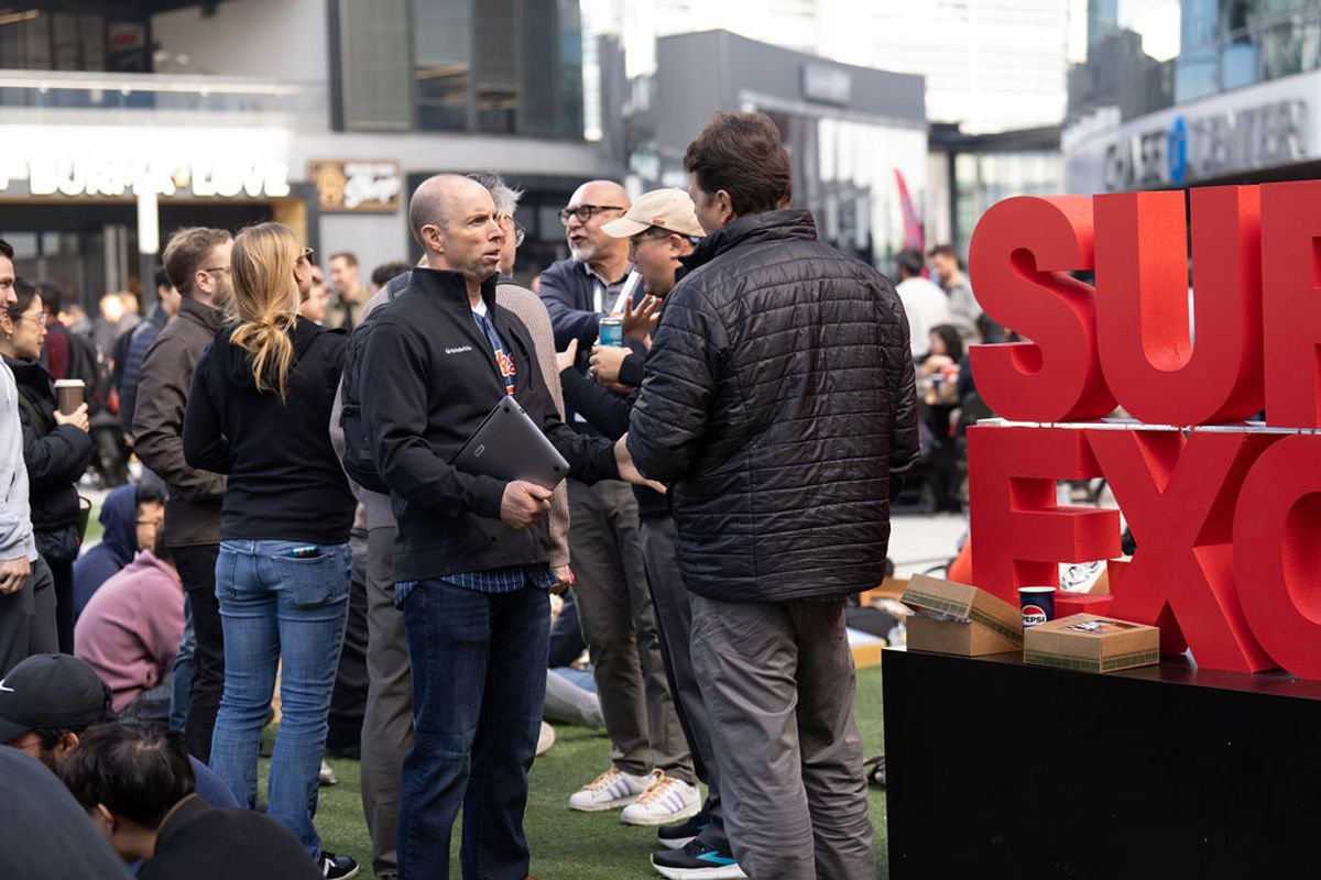 Conference attendees networking and conversing in an outdoor event space with red signage visible