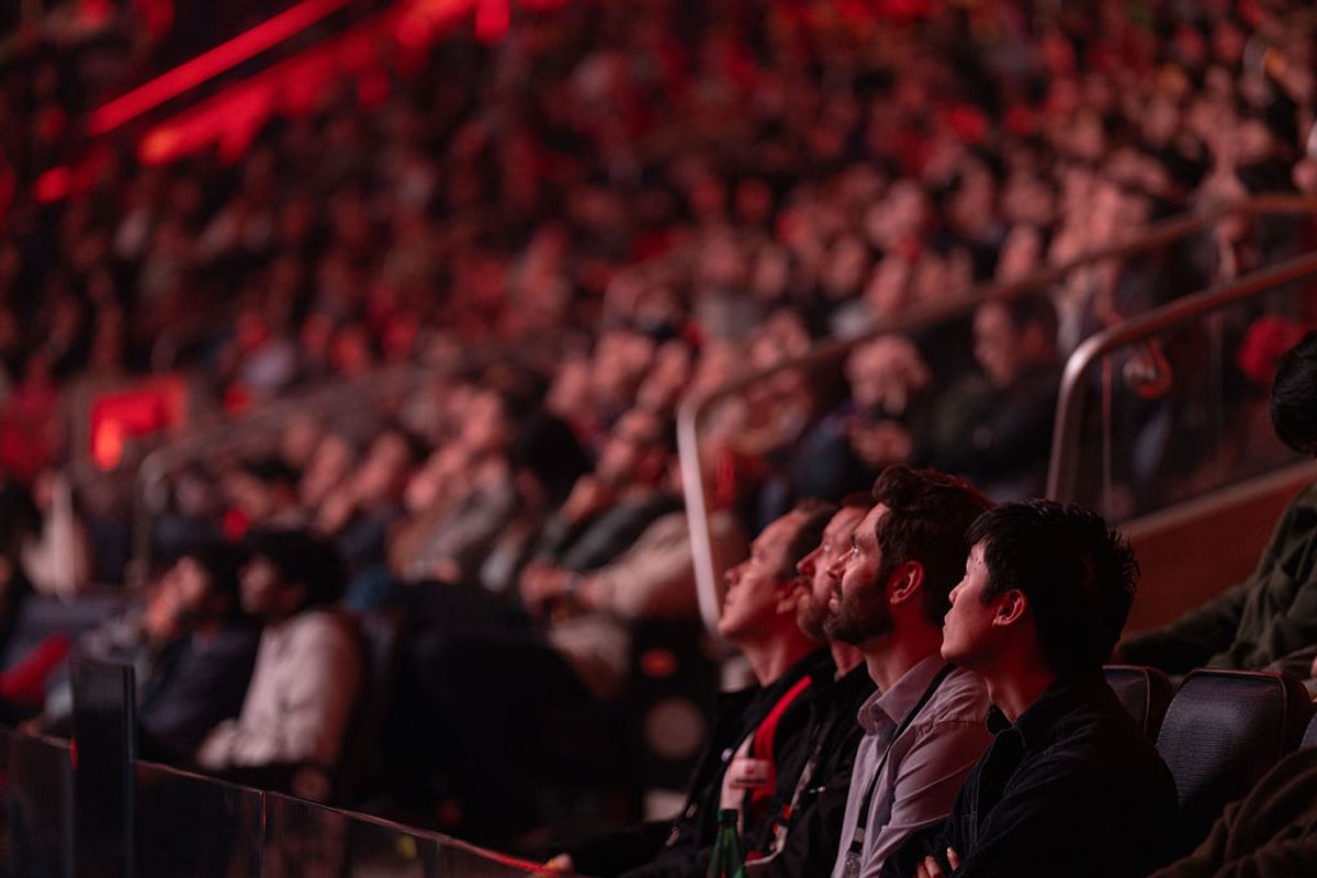 Attendees watching a presentation in a large auditorium with red stage lighting