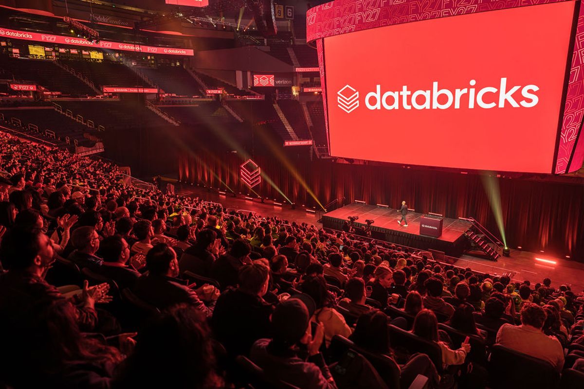 Speaker presenting on stage to seated audience in conference venue with large overhead screen