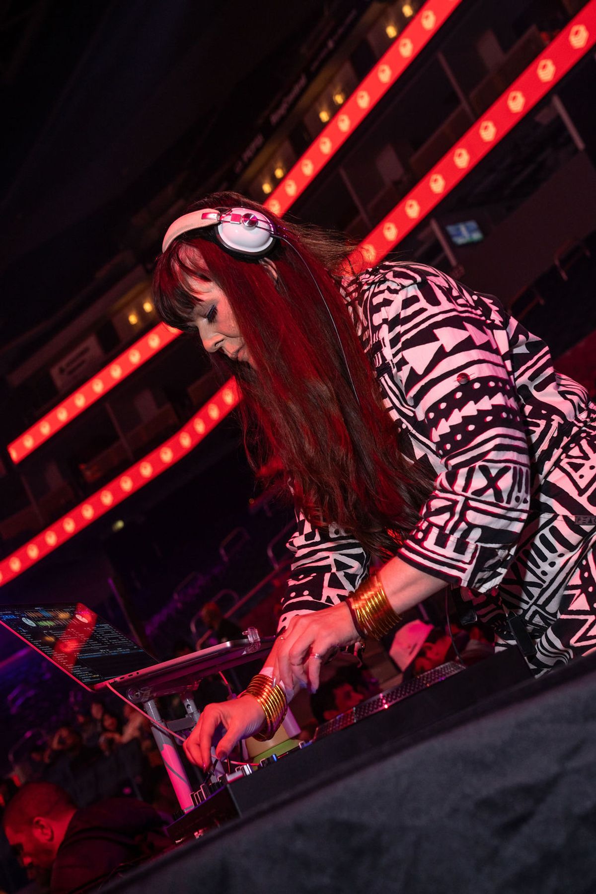 DJ with headphones performing at turntables under red stage lighting at nighttime event