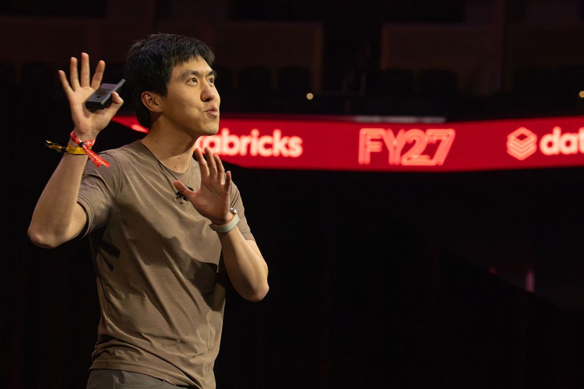 Speaker gesturing with hand raised on stage at conference with red branded backdrop