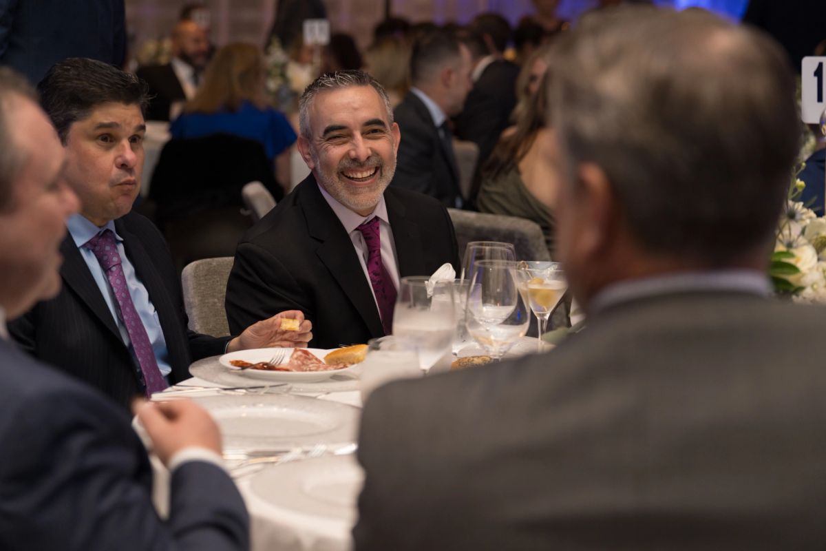 Business executives in suits sitting at dinner table laughing and conversing at formal gala event