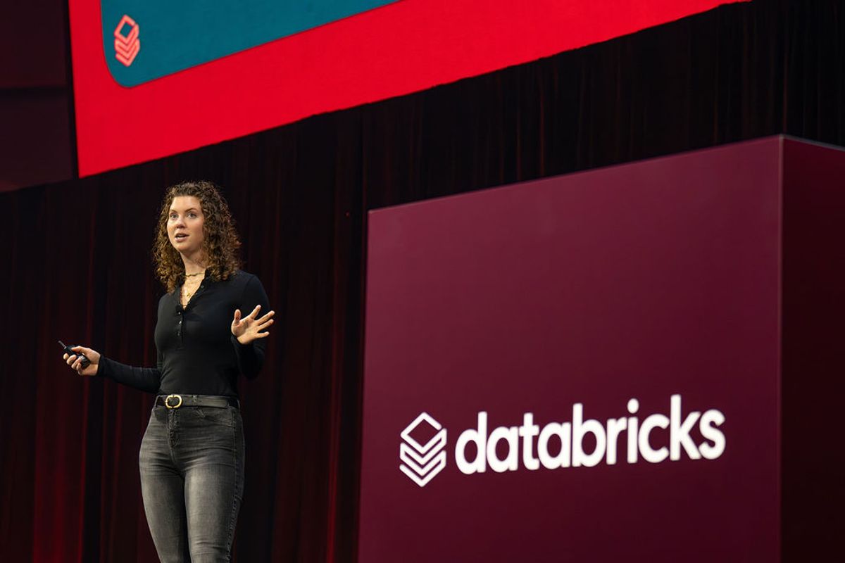Speaker presenting on stage with Databricks logo backdrop at conference venue