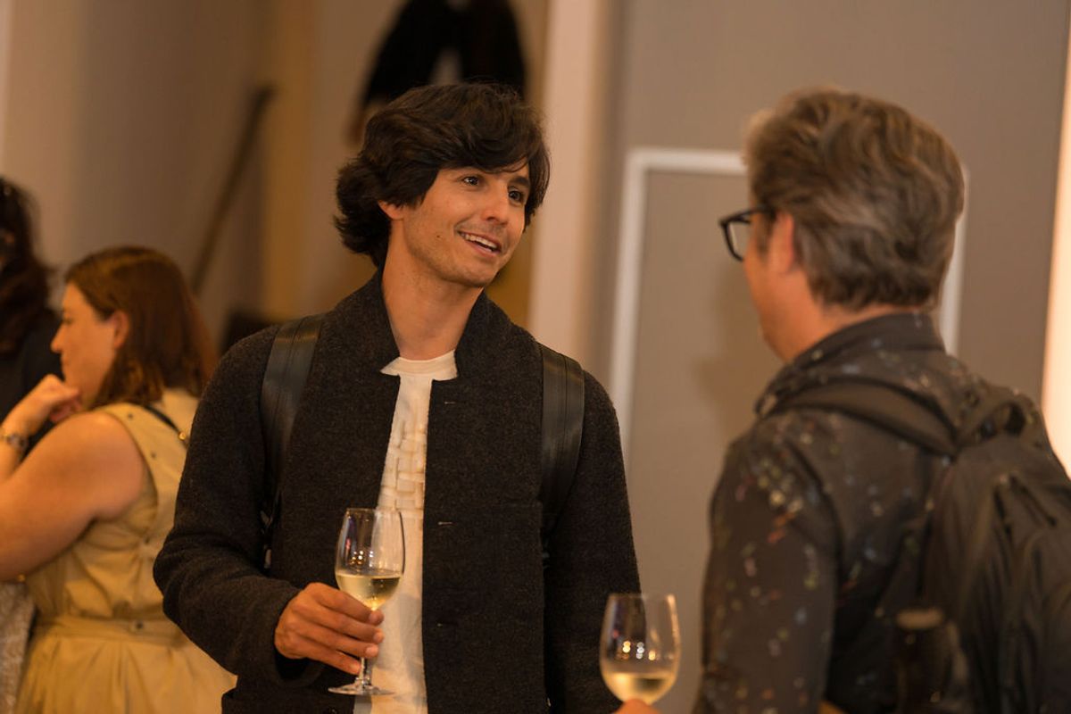 Two men networking with wine glasses at a reception, with other attendees conversing in background