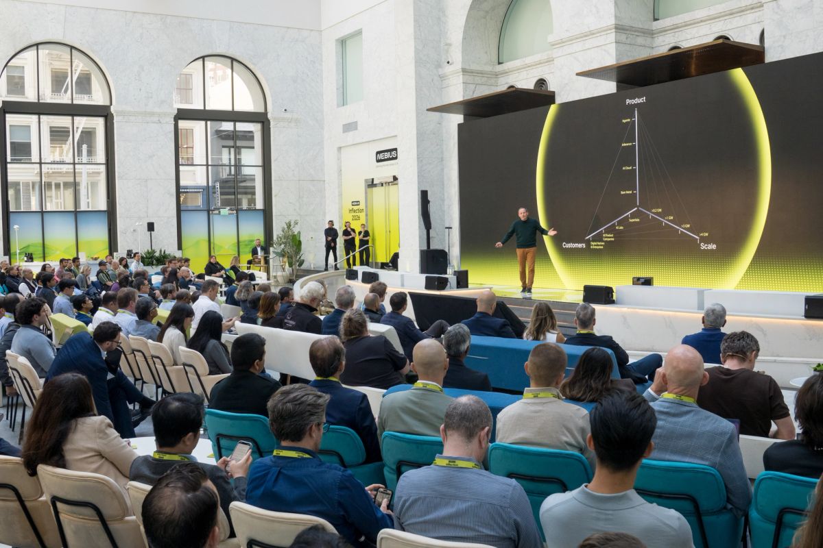 Speaker presents 3D graph on large screen to seated conference audience in bright atrium venue.