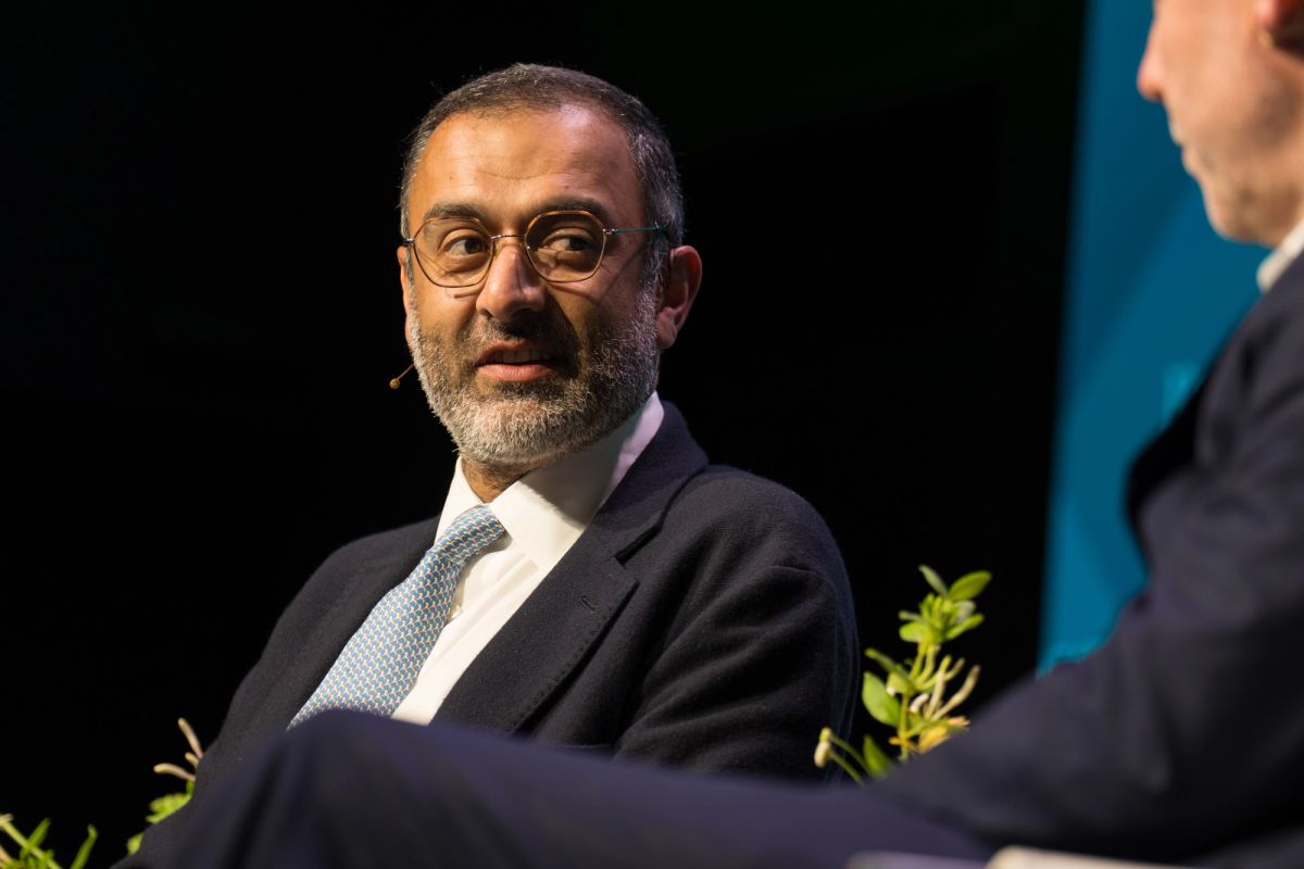 Man in dark suit and glasses sitting during panel discussion with another person partially visible