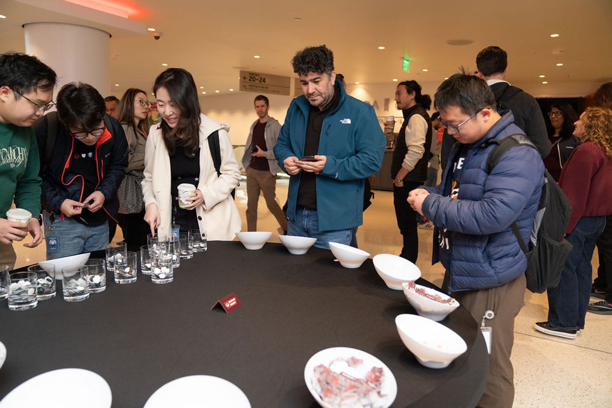 Conference attendees gather around a table with white bowls and glasses, examining items during a networking.