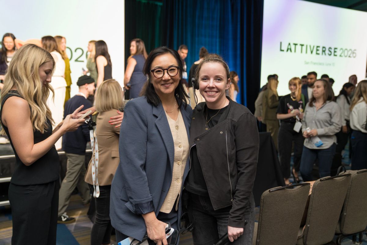 Two attendees smiling at Lattiverse 2026 conference, crowd networking in background.