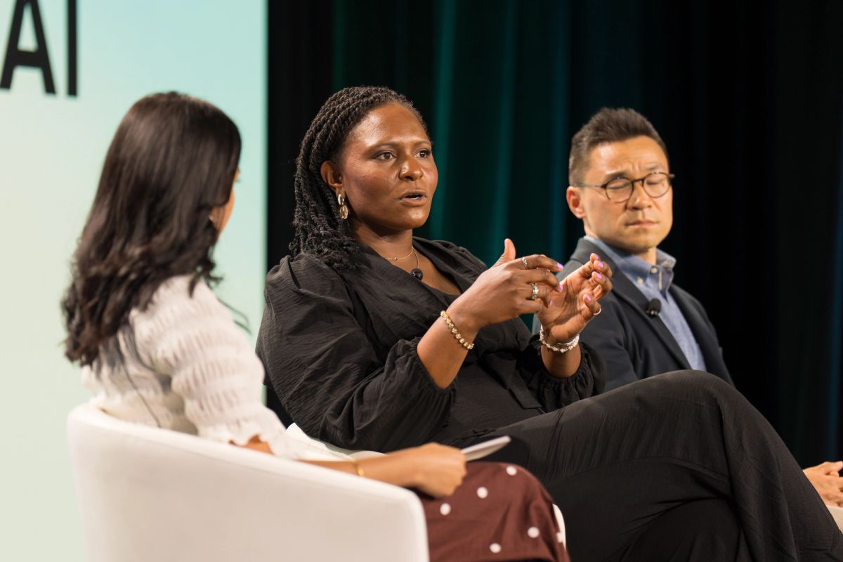 Three panelists in discussion on stage at an AI conference.
