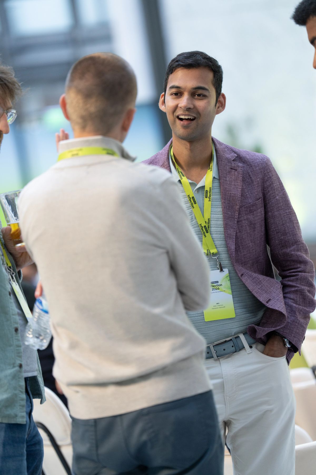 Attendees networking and laughing at an indoor conference event with yellow lanyards.