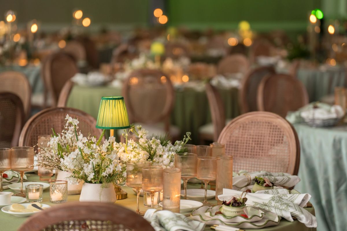 Elegant dining room with round tables set with white flowers, candles, and wicker chairs in warm lighting