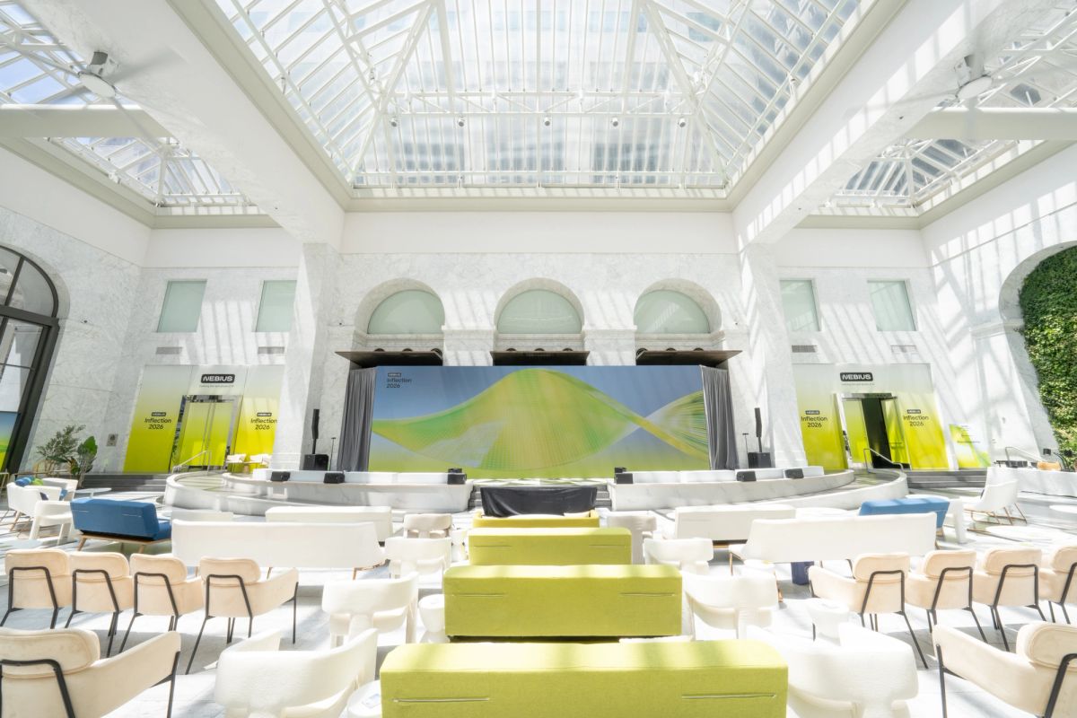 Empty conference hall with green furniture, glass ceiling, and a stage with a large screen display.