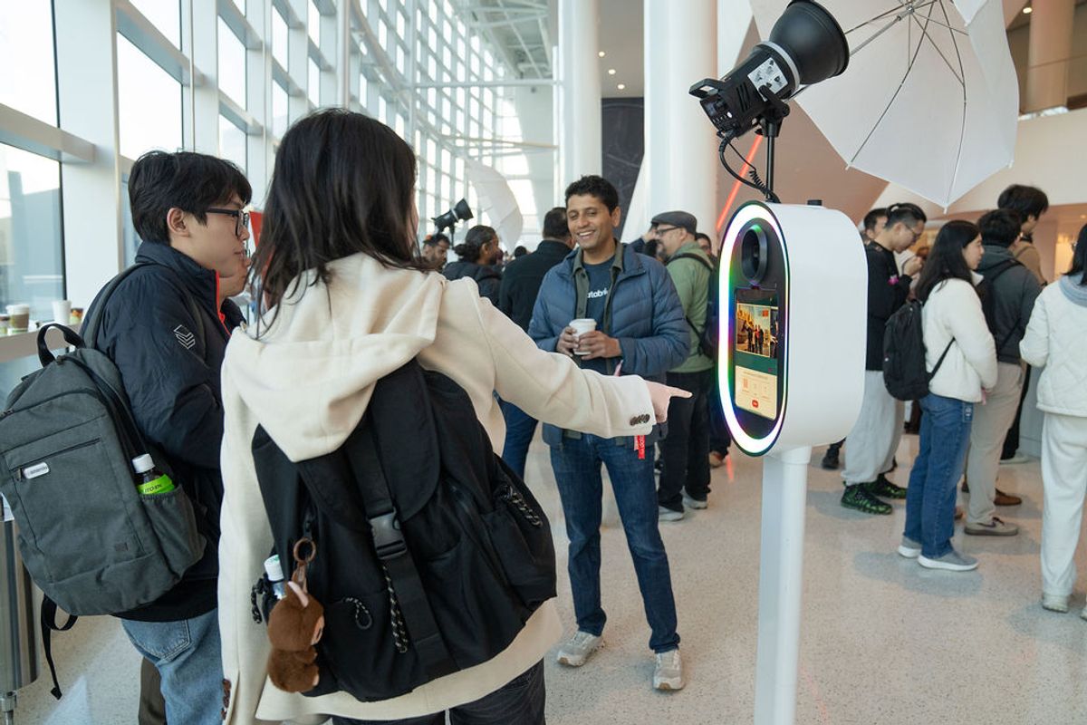 Conference attendees interact with a white robotic kiosk with circular screen in a modern venue lobby